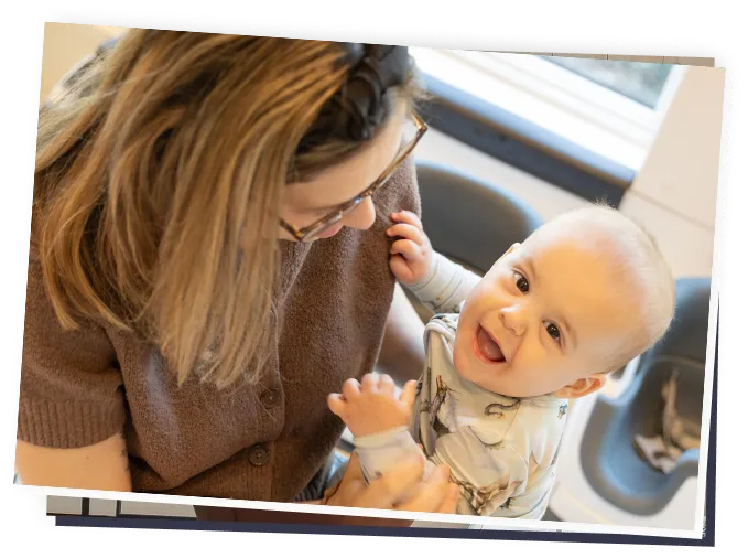 Female caregiver holding smiling infant in childcare setting, engaging in play and bonding