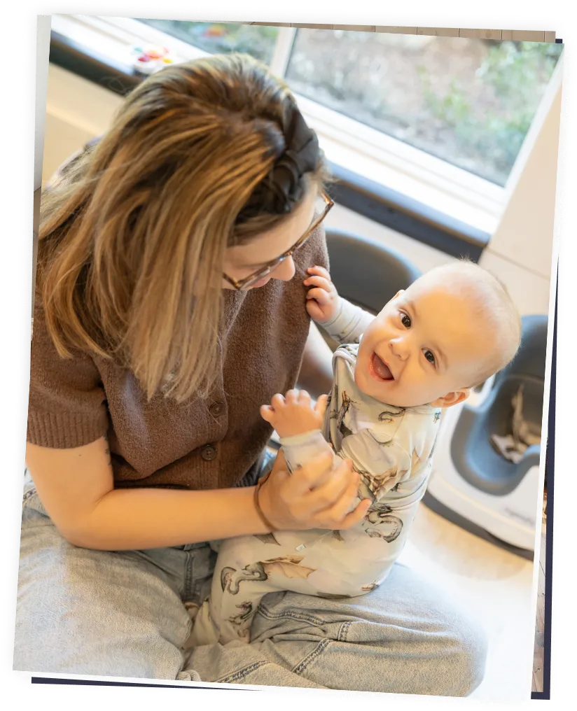Caregiver holding a smiling infant on their lap in a childcare setting, engaging in play.
