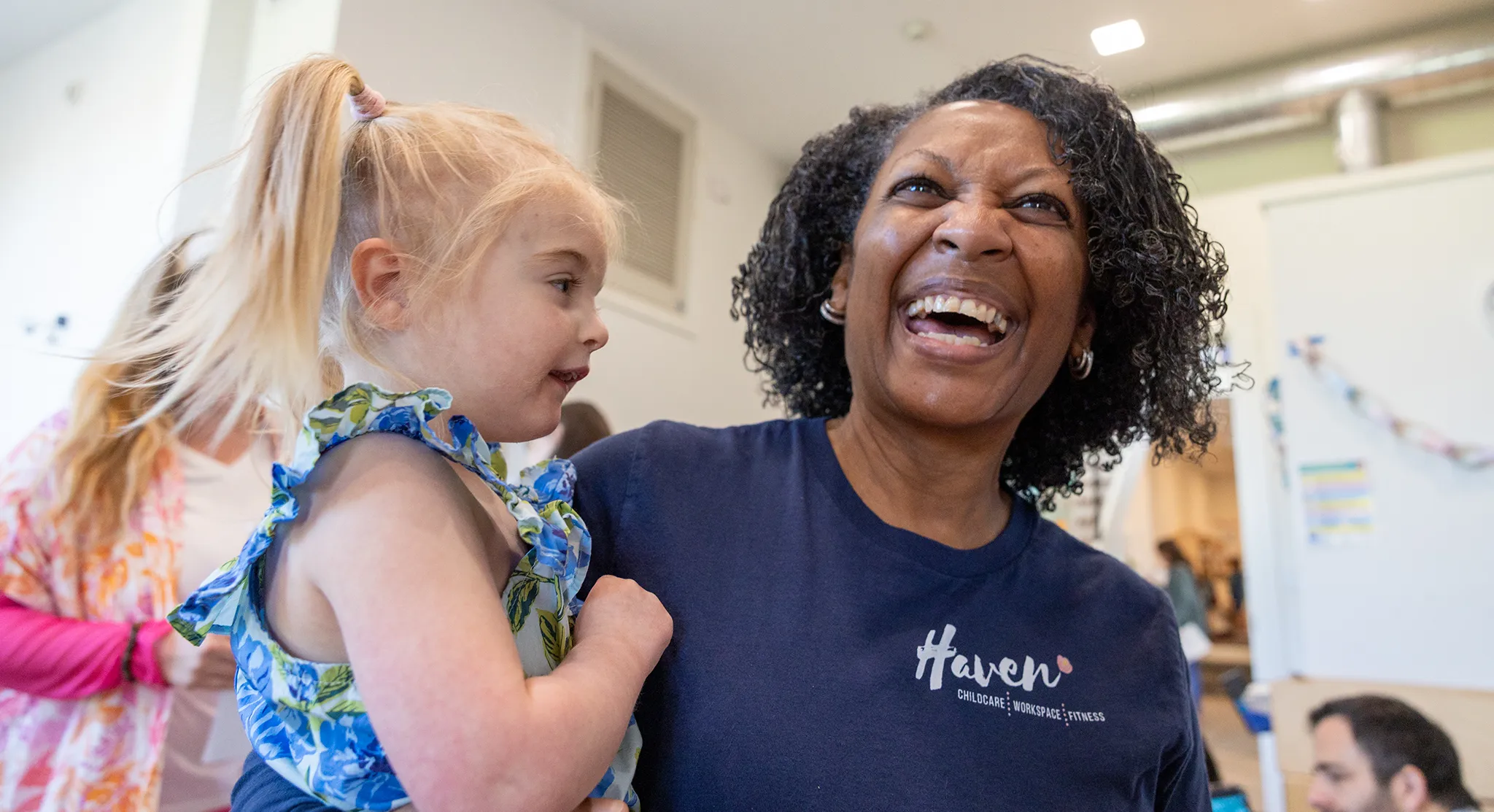 Smiling Haven caregiver holding a toddler, engaging in playful learning at childcare