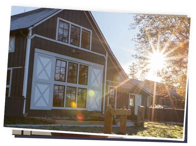Barn-style childcare building exterior with large windows, sun flare and small wooden outdoor play area