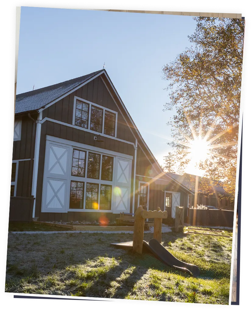Barn-style building with large windows, sun flare and small wooden slide in grassy yard