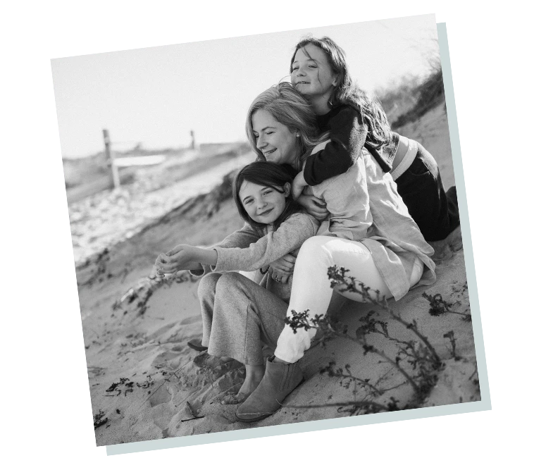 Adult woman and two children sitting on a sandy dune, hugging and smiling, familycare and togetherness